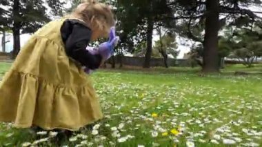 Pelüş tavşanlı küçük bir kız çiçek açan papatyalarla parkta yürüyor. Yüksek kalite 4k görüntü