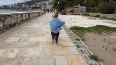 Küçük kız deniz boyunca asfalt gezinti güvertesi boyunca koşuyor. Yüksek kalite 4k görüntü