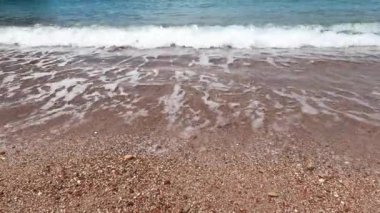 Deniz dalgaları küçük çakıl taşlarıyla kumlu bir sahilde yuvarlanır. Yüksek kalite 4k görüntü