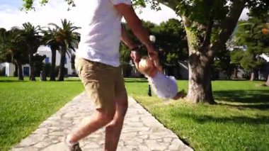 Babam yeşil bir parktaki fayanslı bir yolda küçük bir kızı kollarından döndürür. Yüksek kaliteli FullHD görüntüler