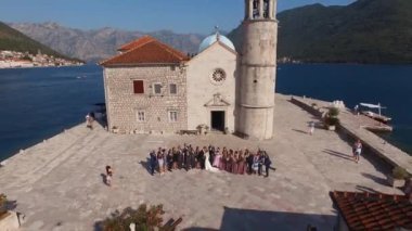 Konukları olan yeni evliler, Gospa od Skrpjela adasındaki Kayalıklar Leydisi Kilisesi 'nin yanında duruyor. Drone. Yüksek kalite 4k görüntü