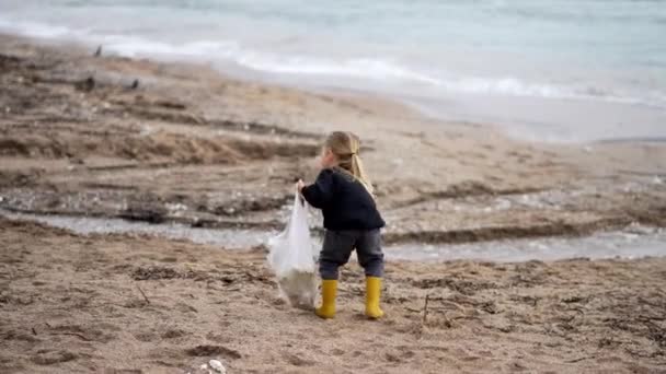 小さな女の子は袋に砂のビーチでペットボトルやカップを収集します 高品質4K映像 — ストック動画