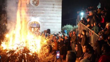 Kalabalık, kilise bahçesindeki dallardan çıkan büyük bir ateşin yanında duruyor. Yüksek kalite 4k görüntü