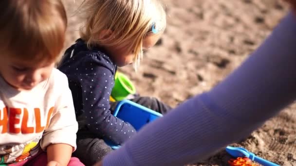 小さな女の子は母親の隣の砂の中でプラスチック製のバケツと型で遊んでいます 高品質4K映像 — ストック動画