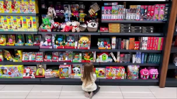 小女孩跪在货架前挑选商店里的玩具 高质量的4K镜头 — 图库视频影像