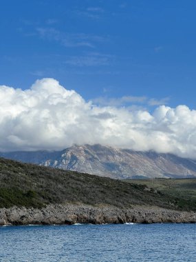 Beyaz kümülüs bulutları deniz kenarındaki yeşil bir dağ sırasına iner. Yüksek kalite fotoğraf