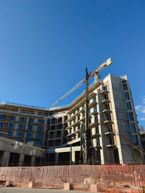 İnşaat vinci çok katlı bir binanın yanındaki çitin arkasında duruyor. Yüksek kalite fotoğraf