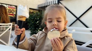 Küçük kız bir eliyle waffle yer, diğer eliyle dondurma külahını tutar. Yüksek kalite 4k görüntü