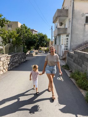 Anne ve küçük bir kız küçük bir kasabanın caddesinde el ele yürüyorlar. Yüksek kalite fotoğraf