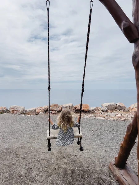 Little girl swings on a rope swing on a mountain above the sea. High quality photo