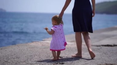 Anne ve küçük bir kız çıplak ayakla iskelede yürür ve denize bakarlar. Kırpılmış. Yüksek kalite 4k görüntü