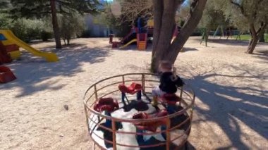 Küçük kız ağaçların arasında bir oyun parkında atlıkarıncaya biniyor. Yüksek kalite 4k görüntü