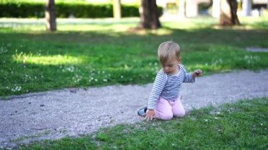 Küçük kız parkta dizlerinin üzerinde yürüyor ve çakıl taşlarıyla oynuyor. Yüksek kalite 4k görüntü