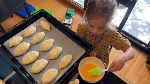 Ένα Κοριτσάκι Βουρτσίζει Χτυπημένα Ψωμάκια Αυγού Ένα Ταψί Υψηλής Ποιότητας — Αρχείο Βίντεο