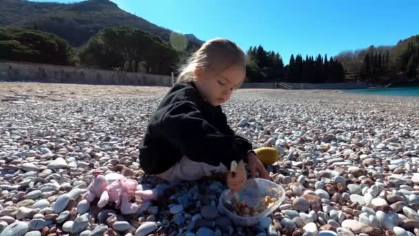 Маленька Дівчинка Сидить Гальковому Пляжі Їсть Кашу Обідньої Коробки Ложкою — стокове відео