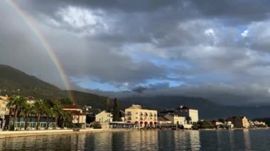 Dağların eteğindeki deniz kıyısındaki evlerin üzerinde gökkuşağı. Yüksek kalite 4k görüntü