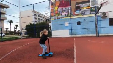 Küçük kız bahçedeki bir basketbol sahasında scooter kullanıyor. Yüksek kalite 4k görüntü