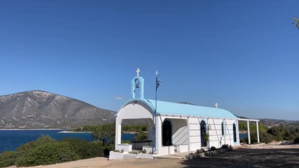 Греческий Флаг Развевается Возле Небольшой Церкви Берегу Моря Фоне Гор — стоковое видео