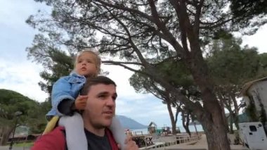 Babası omuzlarında küçük bir kızla deniz kıyısındaki bir tatil köyünün caddesinde yürüyor. Yüksek kalite 4k görüntü