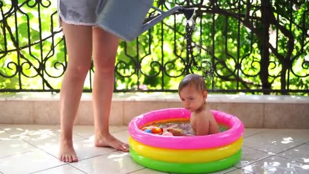 妈妈给坐在阳台上的一个充气游泳池里的小女孩浇水 高质量的4K镜头 — 图库视频影像