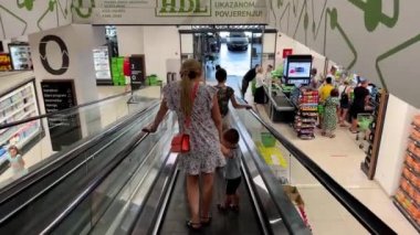 Anne, elinde küçük bir çocukla süpermarkette yürüyen merdivenden aşağı indi. Yüksek kalite 4k görüntü