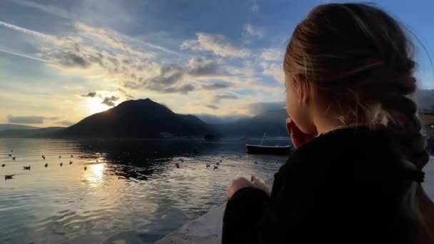 女の子は桟橋でパンを食べ 日没時に海に浮かぶカモメを見ています 高品質4K映像 — ストック動画