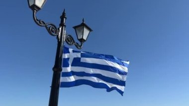 Yunanistan bayrağı mavi gökyüzüne karşı bir fener üzerinde rüzgarda dalgalanıyor. Yüksek kalite 4k görüntü