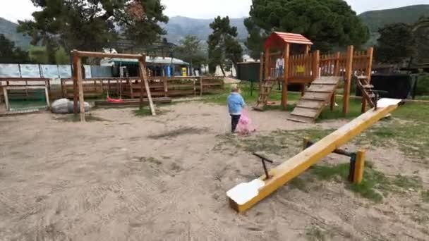Ein Kleines Mädchen Rennt Mit Einem Teddybär Kinderwagen Zur Rutsche — Stockvideo