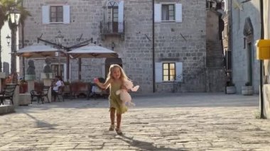 Pelüş tavşanlı küçük bir kız eski kasabanın caddesinde koşuyor. Ağır çekim. Yüksek kalite 4k görüntü