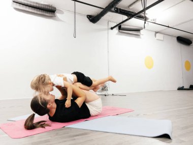 Annem spor salonunda mindere uzanmış küçük bir kızı bacakları üzerinde tutuyor. Yüksek kalite fotoğraf