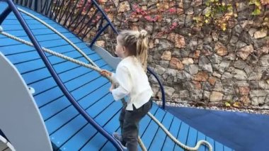 Küçük kız elleriyle ipi tutarak tahta bir kaydırağa tırmanıyor. Yüksek kalite 4k görüntü