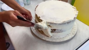 Ev hanımı pastanın kenarlarına spatulayla beyaz krema sürer. Yüksek kalite 4k görüntü