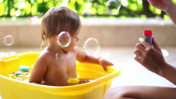 妈妈在阳台上坐在一碗水里的小宝宝身上吹肥皂泡 高质量的4K镜头 — 图库视频影像