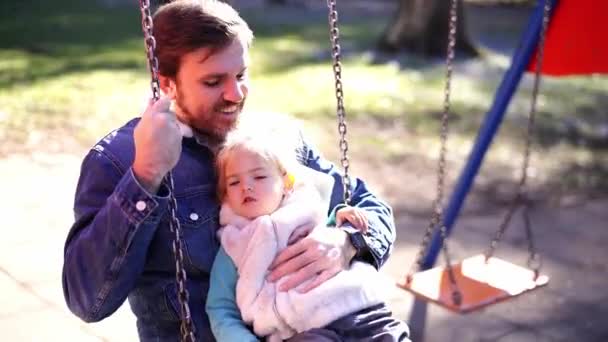 遊び場でチェーンスイングに彼の腕の中で小さな女の子とお父さん 高品質4K映像 — ストック動画