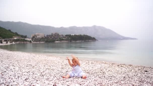 小さな女の子は小石のビーチで小石で遊ぶ 立ち上がって歩く 高品質4K映像 — ストック動画