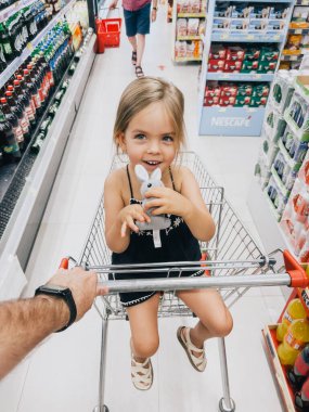 Babam elinde pelüş bir tavşanla küçük bir kızı süpermarket arabasında taşıyor. Yüksek kalite fotoğraf