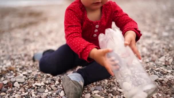 Little Girl Collects Pebbles Puts Them Bottle While Sitting Beach — Stock Video