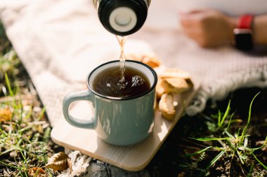 Kahve termostan bir fincana dökülüyor çimenlikteki ahşap bir tahtanın üzerinde duruyor. Yüksek kalite fotoğraf
