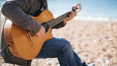 Müzisyen sahilde bir sandalyede otururken akustik gitar çalar. Kırpılmış. Yüzsüz. Yüksek kalite fotoğraf