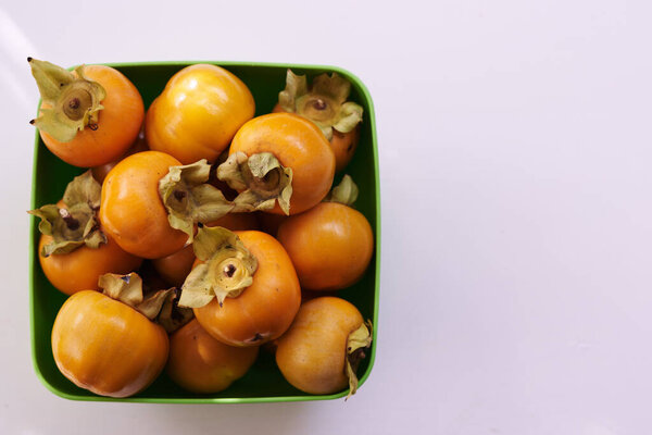 Bunch of ripe persimmons lies in a square green bowl on a white table. Top view. High quality photo