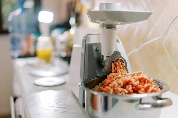 Electric meat grinder twists meat into a pan on a kitchen table. High quality photo