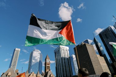 Toronto, Kanada - 28 Ekim 2023: Filistin bayrağı gökdelenler ve arka planda dik duran eski bir saat kulesi ile şehrin silueti arasında dalgalanıyor. Yüksek kalite fotoğraf