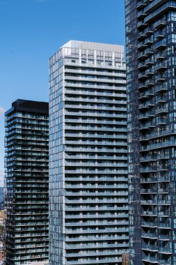 Açık mavi gökyüzü altında cam cepheli modern gökdelenler, güneş ışığını yansıtıyor. Yüksek kalite fotoğraf