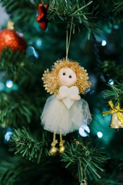 Kalbi olan bir meleğin heykeli parlak çelenklerin yakınındaki bir Noel ağacının dalına asılı. Yüksek kalite fotoğraf