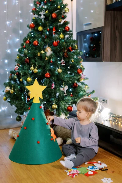 Küçük kız oyuncak Noel ağacına oyuncaklar asıyor odanın zemininde oturuyor. Yüksek kalite fotoğraf
