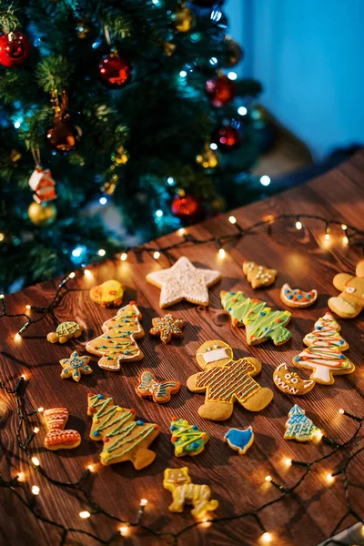Glazed cookies lie on the table among luminous garlands near the decorated Christmas tree. High quality photo