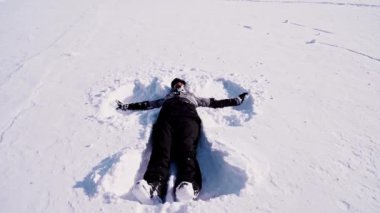 Kız kar yığınına yatar ve elleri ve ayaklarıyla bir kar meleği yapar. Yüksek kalite 4k görüntü
