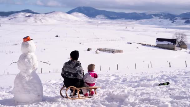 Anya Egy Kisgyerekkel Egy Szánkón Egy Hóember Mellett Visszanézni Kiváló — Stock videók