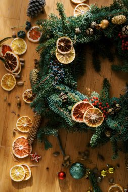 Kurumuş portakal parçaları ve köknar kozalakları ahşap bir zeminde bir Noel çelenginin yanında yatıyor. Kırpılmış. Yüksek kalite fotoğraf