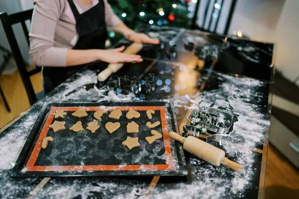 Cook rolls out the dough on the table next to the tray with cut out cookies. Cropped. High quality photo